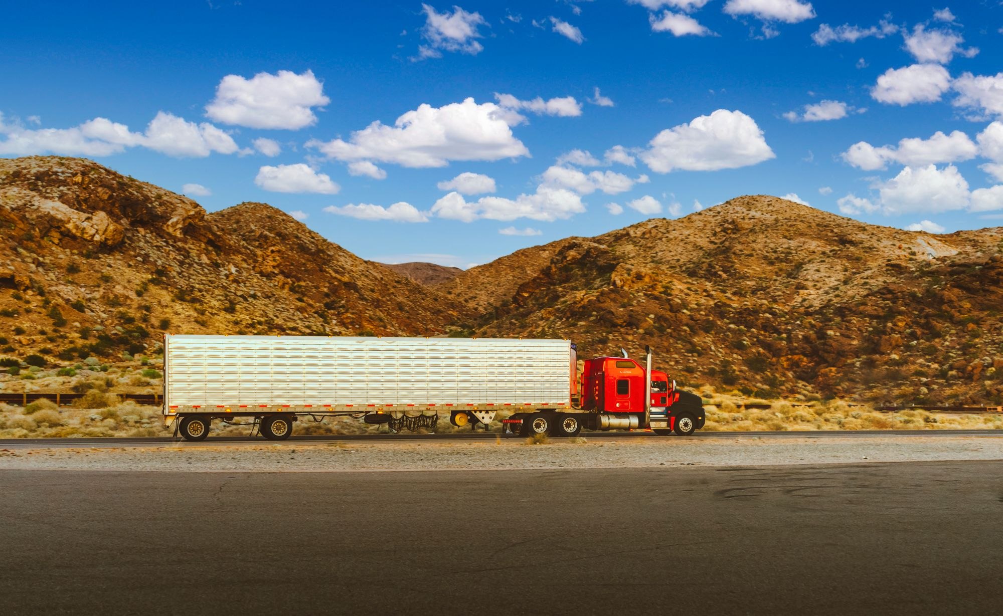 Red American semi truck hauling a trailer along an arid highway